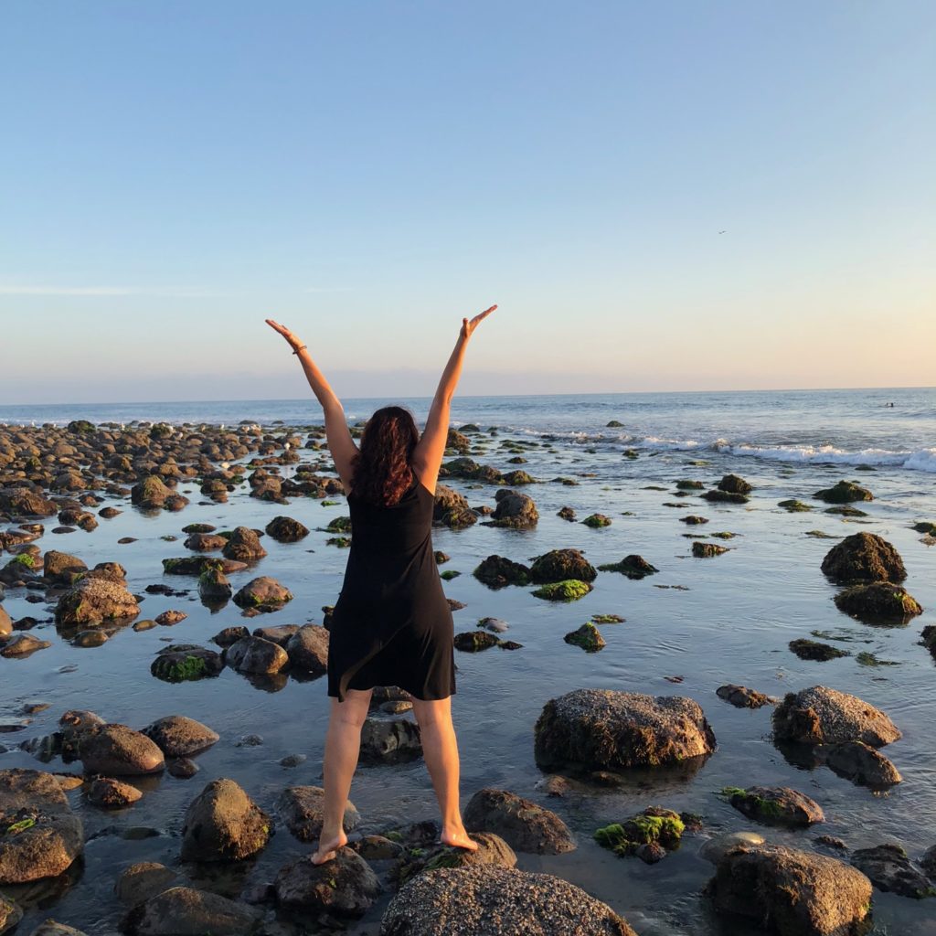 Back of woman arms outstretched to sky on a rocks shore