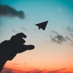 Silhouette of hand throwing paper airplane into the sunset and clouds